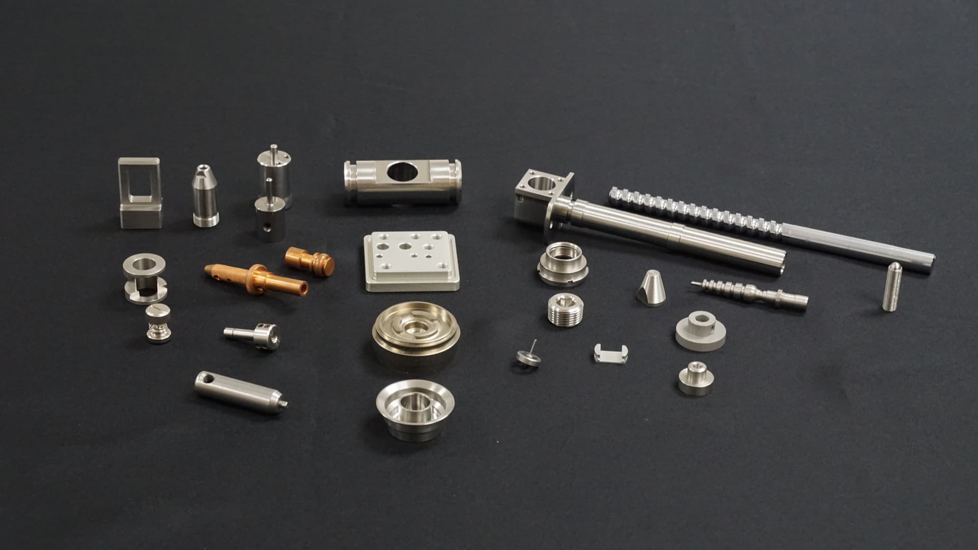 A range of different CNC machined metal parts placed on a table with black background, showcasing prototype machining