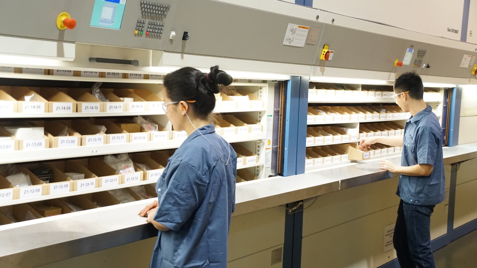 Technicians picking precision CNC machined parts from automated vertical storage system